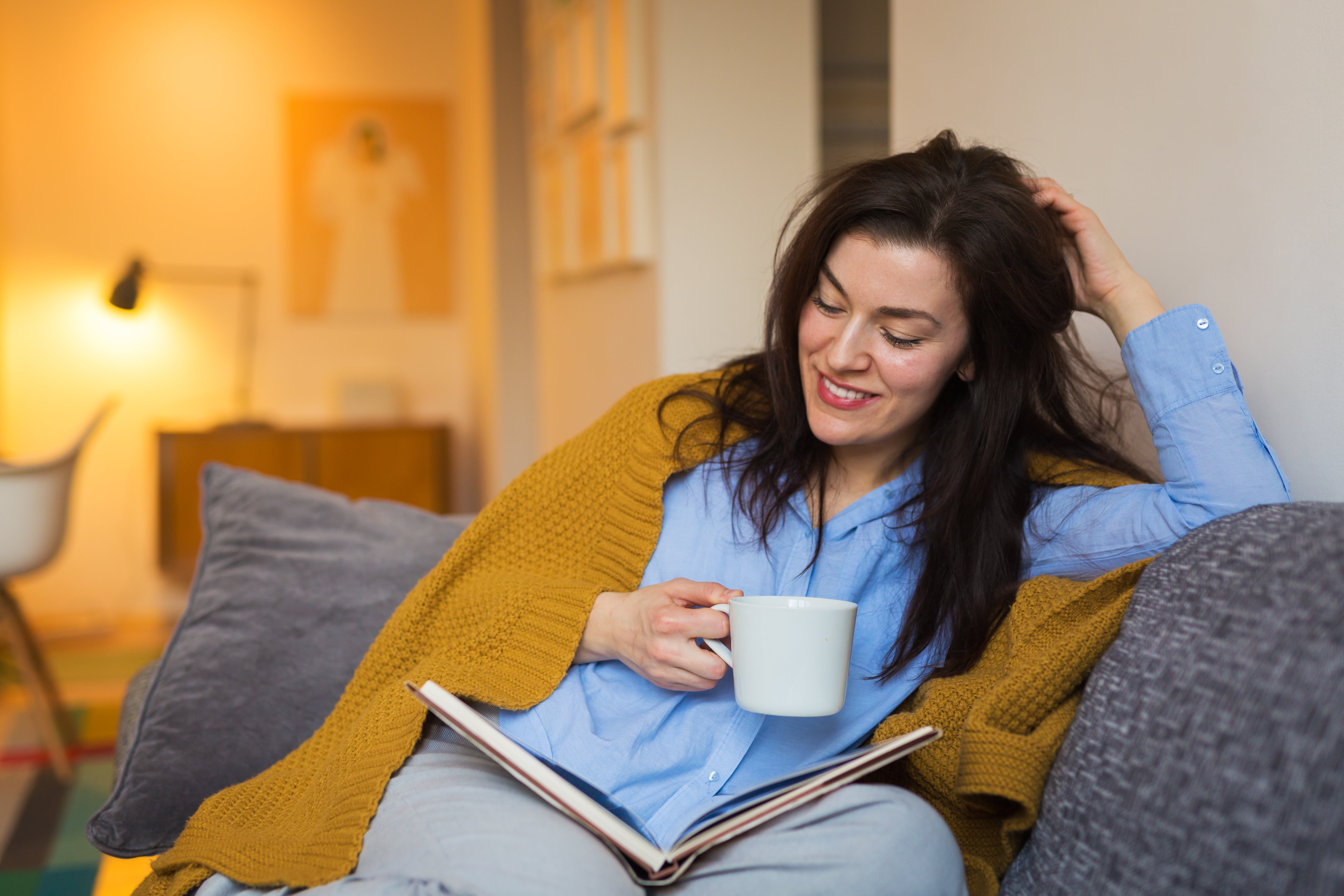 A woman on the couch with a cup of tea and a book