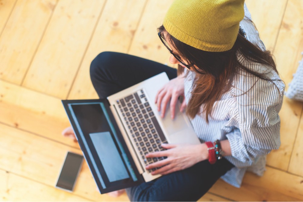 A student working on her laptop while sitting on the floor